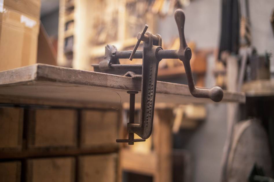 Professional woodworker using heavy-duty bar clamps on a workbench with raw lumber and tools nearby
